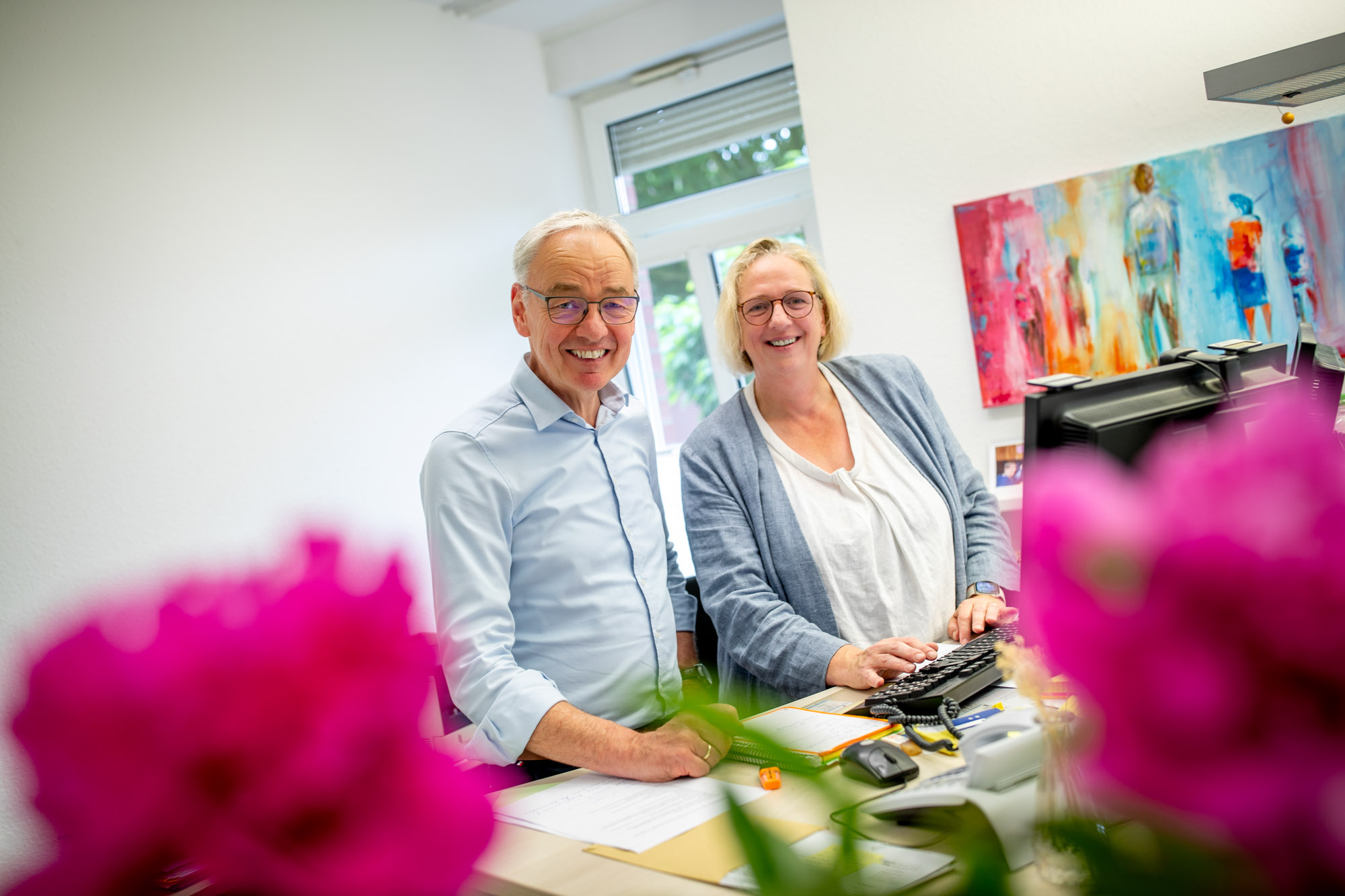 Ein Mitarbeiter und eine Mitarbeiterin stehen lächelnd an einem Schreibtisch im Büro.